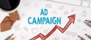 Illustratie met de tekst "Ad Campaign", een stijgende rode pijl, potloden, koekjes en een koffiekopje.