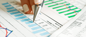 Hand wijst met pen naar blauwe en groene grafieken op een rapport met data.