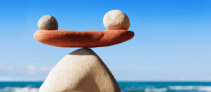 Gebalanceerde stenen op een strand met blauwe lucht, symbool voor balans in unieke verkooppropositie.