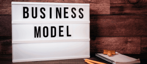 Lightbox met de tekst "Business Model" tegen een houten achtergrond, naast een notitieblok en potloden.