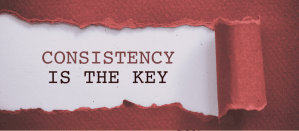 De tekst "Consistency is the key" geschreven op wit papier met een gescheurde rode rand.