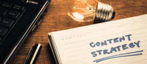 Notitieboek met de tekst "Content Strategy", een lamp en een laptop op een houten tafel.