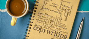 Notitieboek met woordenwolk rond copywriting, naast een kop koffie en een pen op blauwe achtergrond.