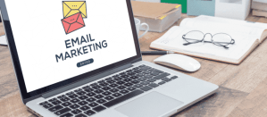 Laptop met 'Email Marketing' op het scherm, omringd door een notitieboek en bril.