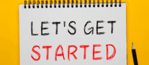Notitieblok met de tekst "Let's Get Started" in zwarte en rode letters op een gele achtergrond.