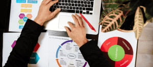 Handen op laptop met marketinggrafieken en strategische plannen op tafel.