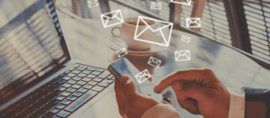 Hand bedient smartphone met digitale e-mailnotificaties, naast een laptop en een kop koffie.