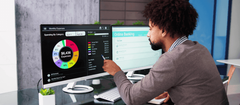 Man wijst naar een financieel dashboard op een computerscherm met uitgavenanalyse.