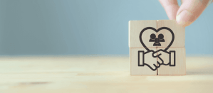 Handdruk en een hart met menseniconen op houten blokken, symbool voor samenwerking en relaties.