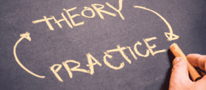 Hand schrijft met krijt op een zwart bord de woorden 'Theory' en 'Practice' met pijlen ertussen.