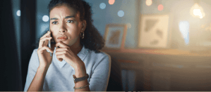 Een bezorgde vrouw voert een telefoongesprek terwijl ze nadenkt, met een huiselijke achtergrond.