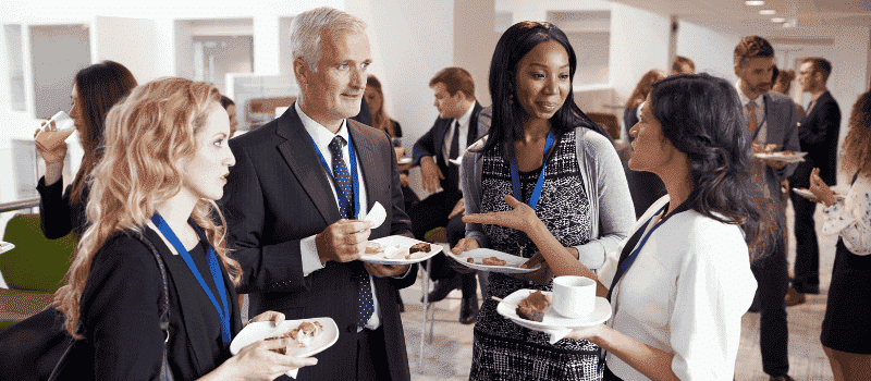 Groep professionals in gesprek tijdens een zakelijk netwerkevenement met eten en drinken.