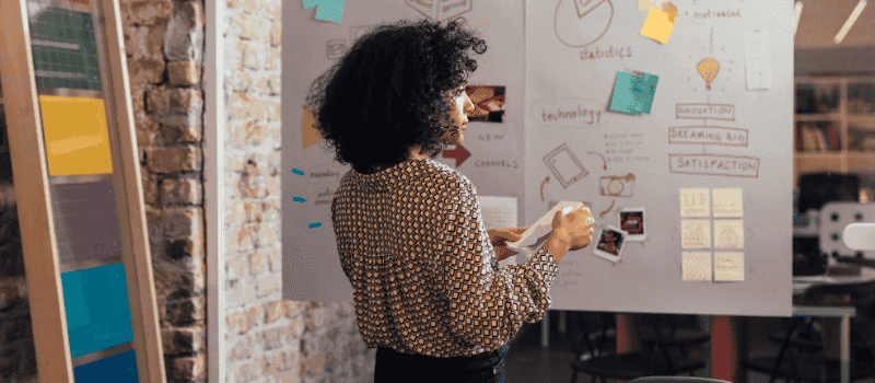 Een persoon met zwart, krullend haar bekijkt een moodboard met markering, foto's en notities over innovatie en technologie.