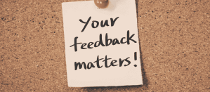 Papieren notitie met de tekst "Your feedback matters!" op een kurken prikbord.