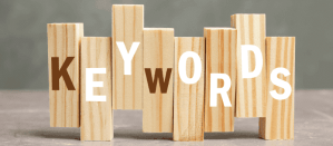 Houten blokken vormen het woord "KEYWORDS" op een grijze achtergrond.