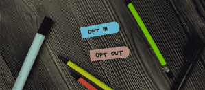 Blauwe en bruine labels met de teksten "OPT IN" en "OPT OUT" op een houten bureau met pennen en markers.