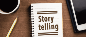 Open notitieboek met de tekst "Storytelling" naast een potlood, koffie en tablet op een houten bureau.