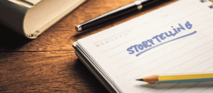 Open notitieboek met het woord "Storytelling" geschreven in blauw, naast een potlood en pen op een houten bureau.